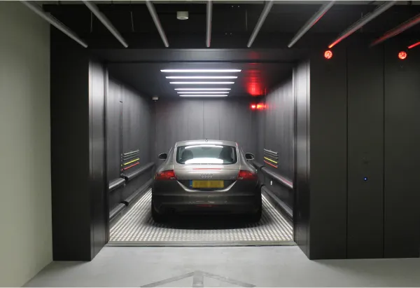A gray car (Audi TT) parked inside a modern car elevator with dark walls and illuminated ceiling lights.