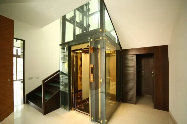 Modern glass home elevator with golden interior installed in a luxury residential space.