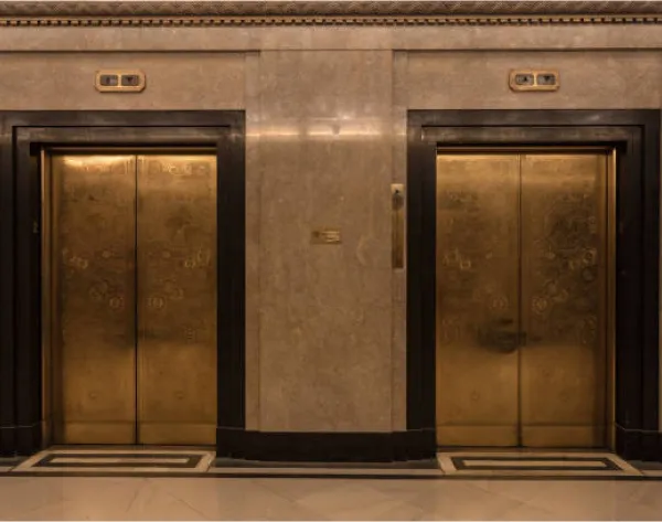 Ornate brass passenger elevator automatic doors in a luxurious or historic building lobby with polished stone walls.