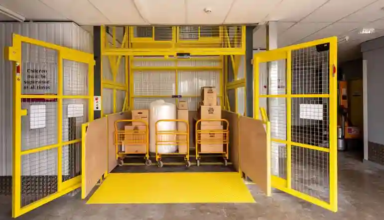 Hydraulic goods lift with safety gates, carrying boxes and trolleys for industrial material handling.